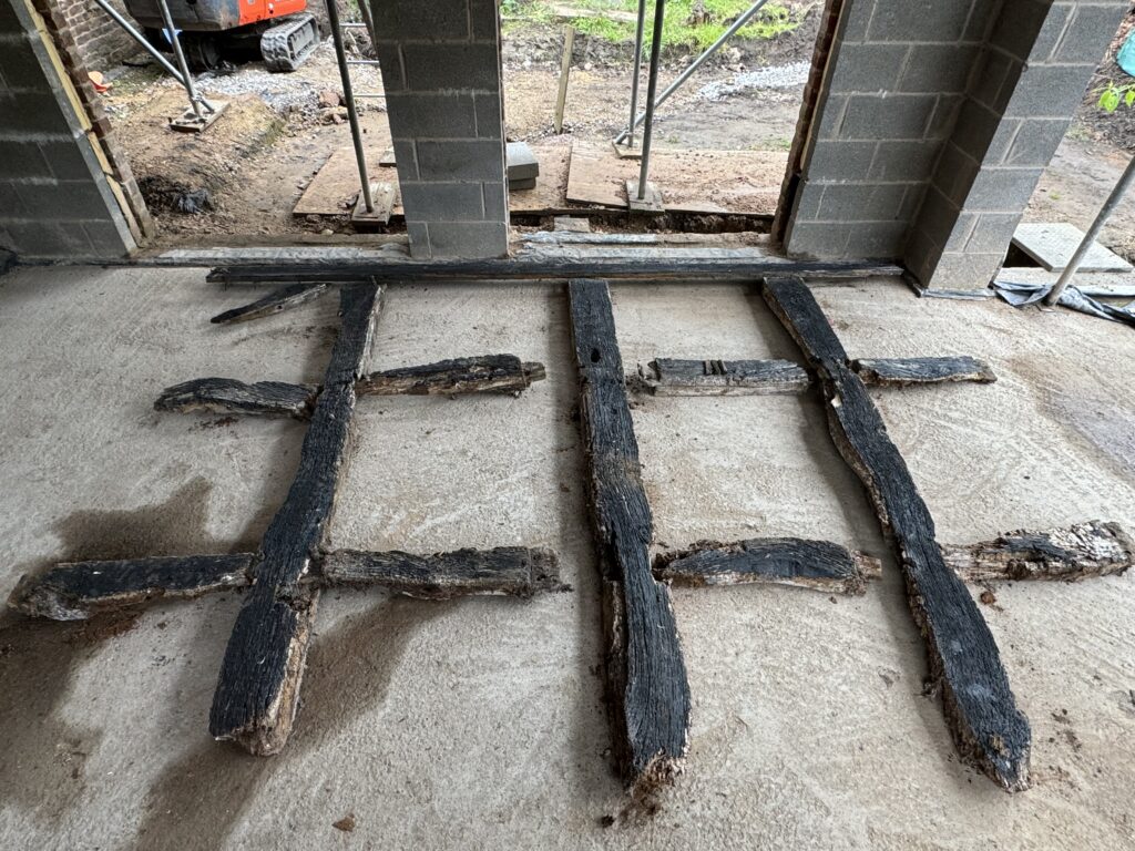 Three charred wooden beams with crosspieces are laid out on a concrete floor inside a partially constructed or renovated building with exposed cinder block walls and open doorways.