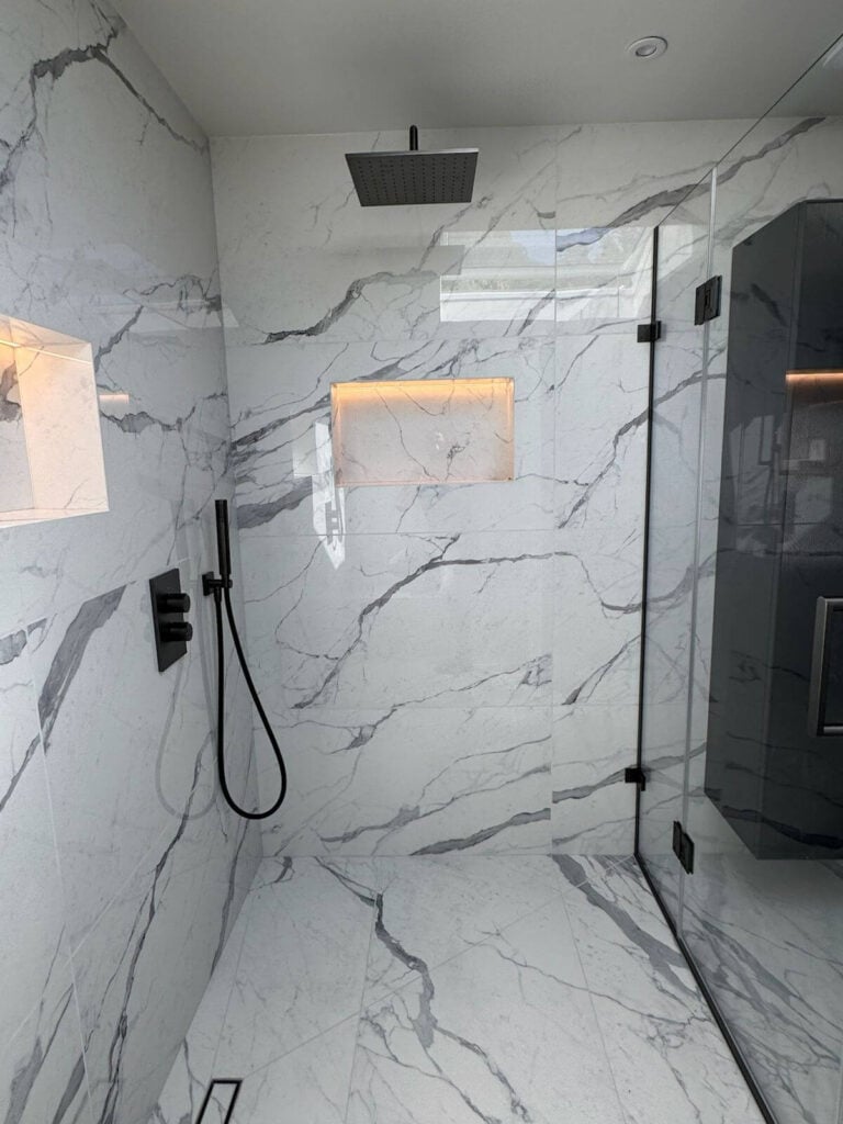 Modern shower with white marble walls and floor, black rainfall showerhead, black fixtures, glass door, and built-in niches with warm lighting.