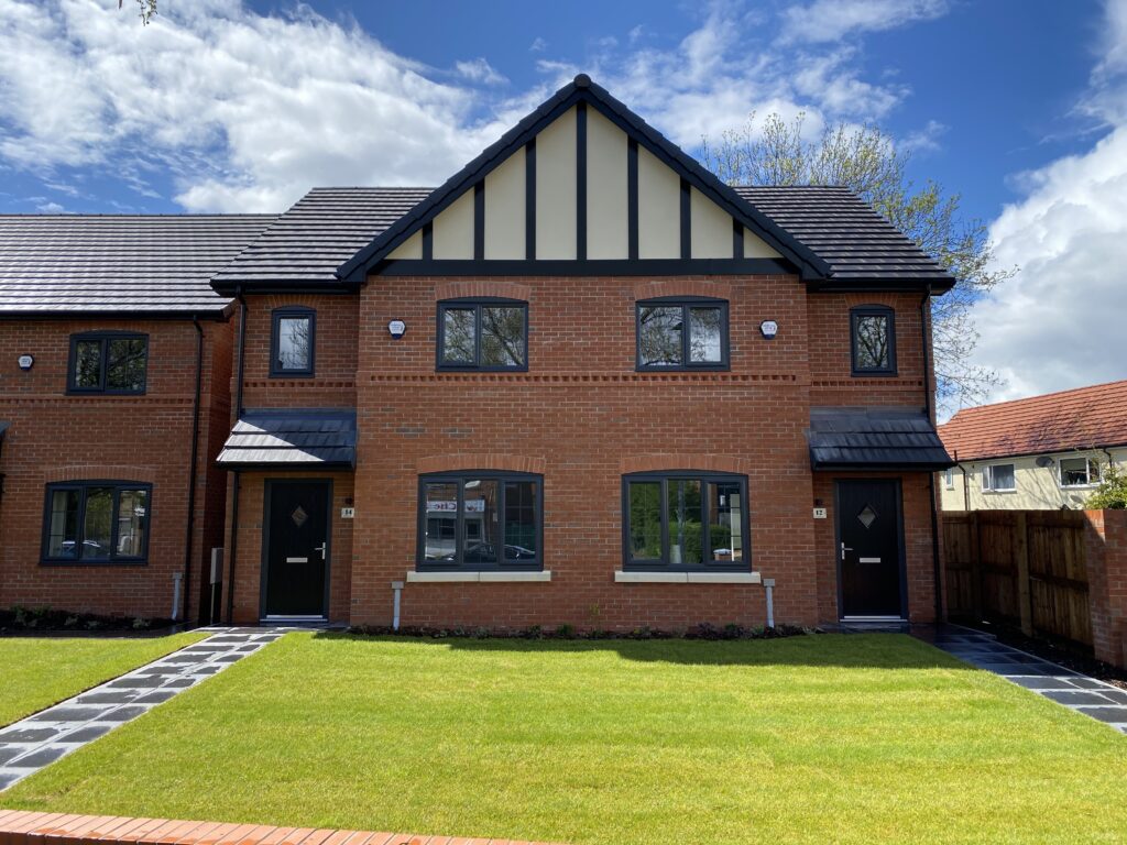 A modern, two-story brick townhouse with a gabled roof and black trim. There are two front doors, symmetrical windows, and a well-maintained lawn with paved walkways leading to each entrance.