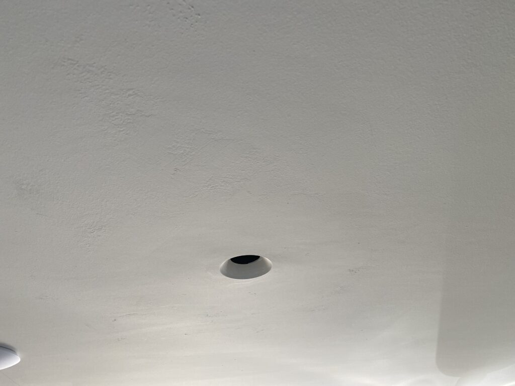 A white ceiling with a single recessed light fixture that does not have a bulb or cover installed. The surface appears smooth with subtle texture.