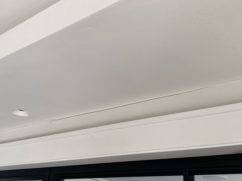 A ceiling with a long, thin crack running across it, next to a recessed light fixture and a dark-framed window or door at the bottom edge.