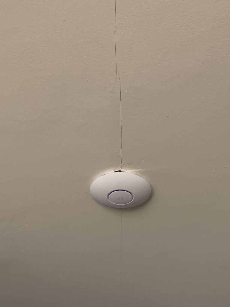 A white circular device is mounted on a beige ceiling with a visible crack running vertically through the ceiling and through the device.