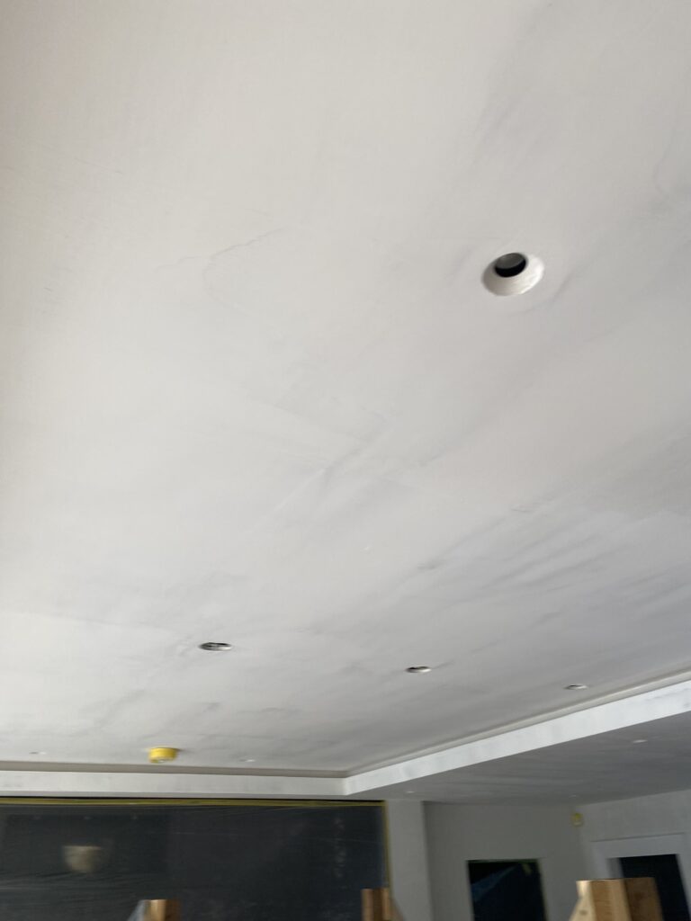 A white ceiling with several recessed light fixtures, some without bulbs. Part of the room's upper walls and a dark section of a chalkboard or wall can be seen below the ceiling.