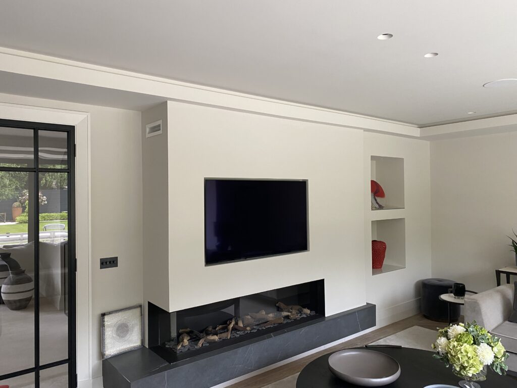 Modern living room with a wall-mounted TV above a sleek fireplace, built-in shelves displaying red vases, a black-framed glass door, and a coffee table with a decorative bowl and a bouquet of flowers.