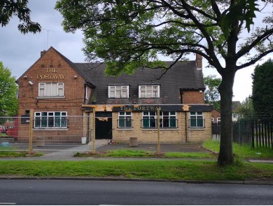 A boarded-up, brick building called "The Portway" stands behind a fence, with overgrown grass and a large tree in front, under a cloudy sky.